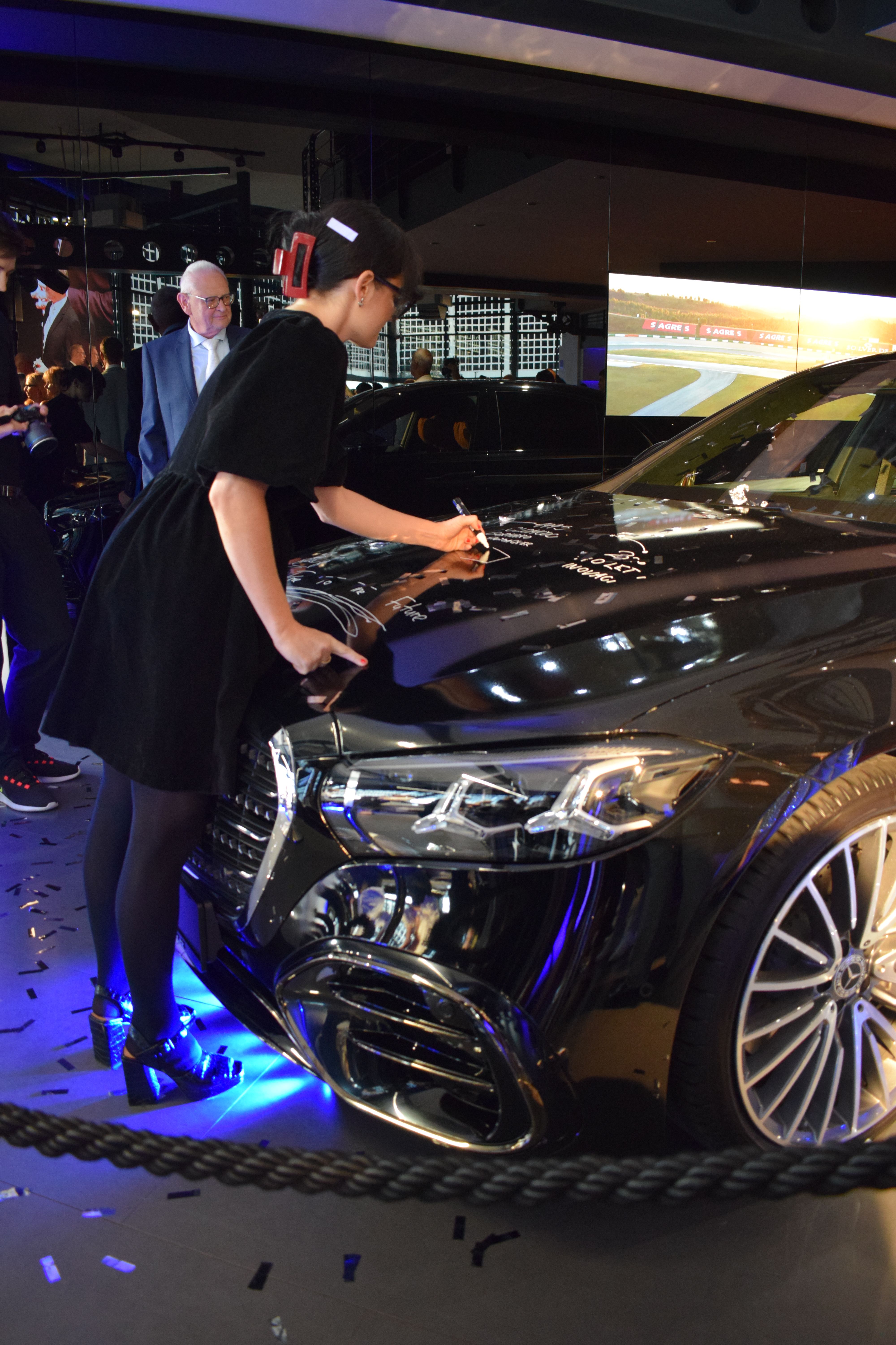 Fashion illustrator creating a live painting with a white POSCA marker on a Mercedes-Benz vehicle during the Drive to the Future event in Olomouc.