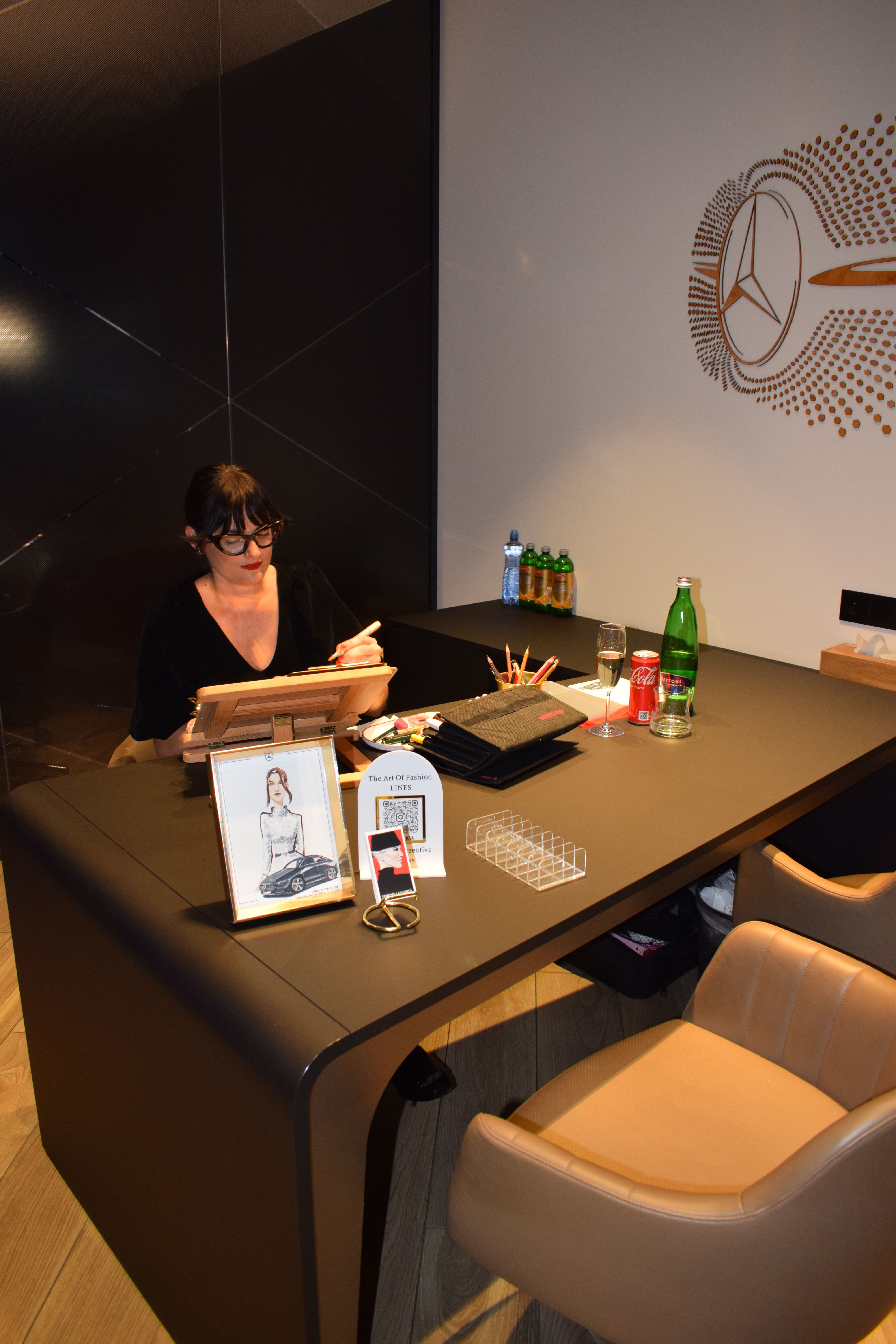 Fashion illustrator creating live sketches during a Mercedes-Benz Moravia event in Olomouc, surrounded by art supplies and illustration samples.